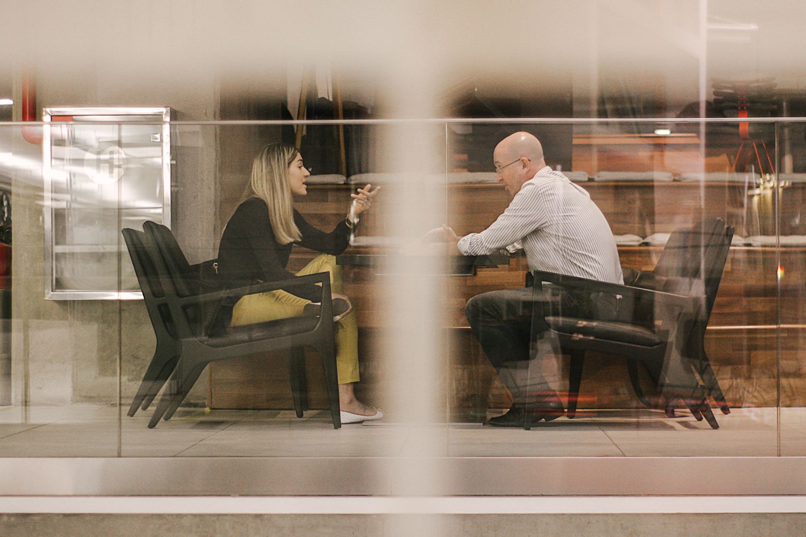 Two professionals talking in a glass-walled conference room.